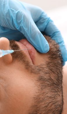 Unrecognizable bearded man getting lips filler at aesthetic clinic, copy space. Closeup of businessman having beauty injection at male spa salon. Face care, anti-aging treatment for men concept